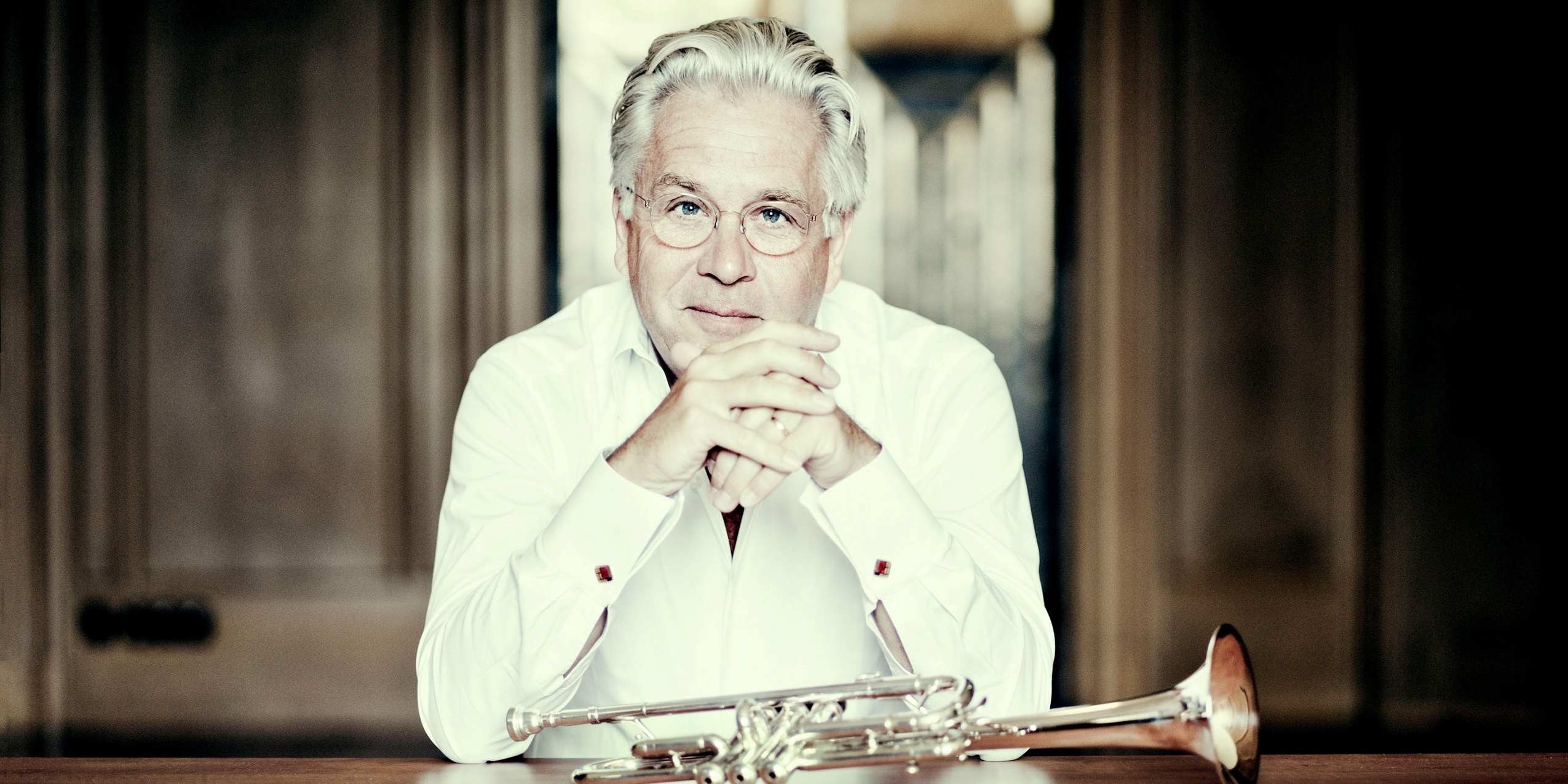Mand i hvid skjorte sidder ved et bord med en trompet liggende foran sig.