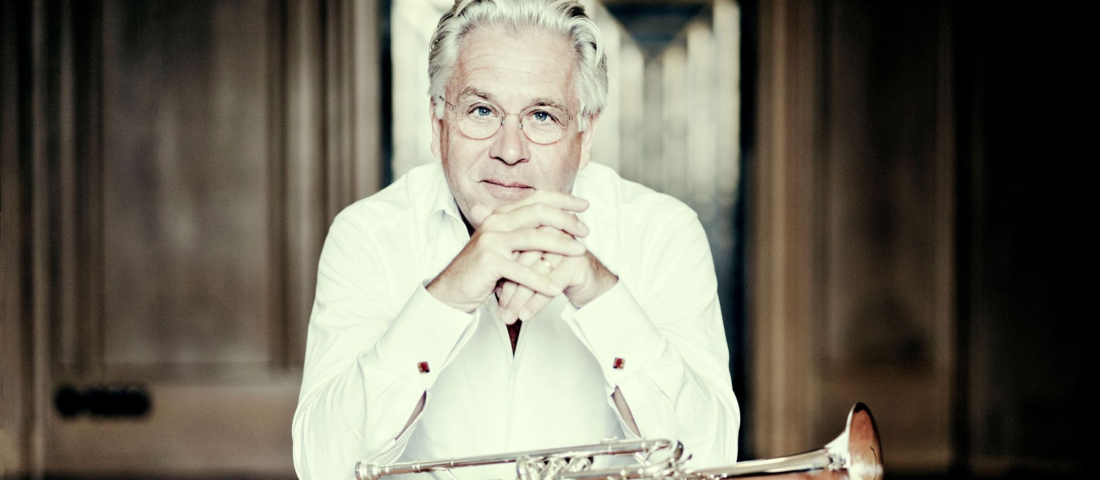 Mand i hvid skjorte sidder ved et bord med en trompet liggende foran sig.