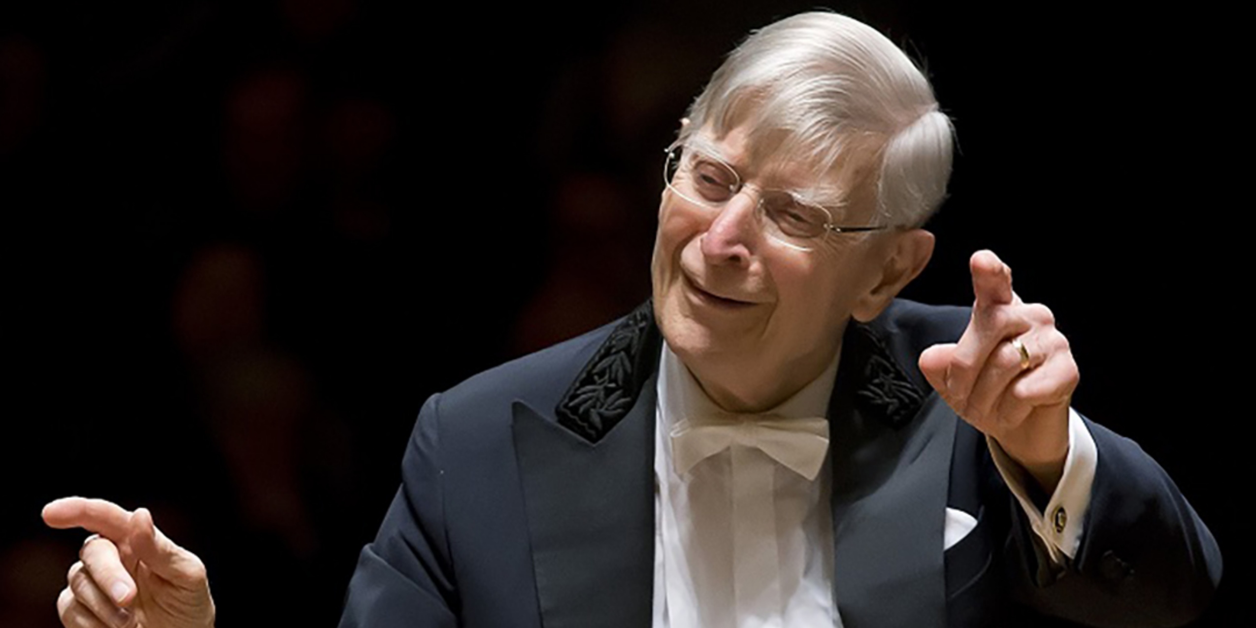 Mand i sort blazer, hvid skjorte og hvid butterfly, dirigere orkesteret.