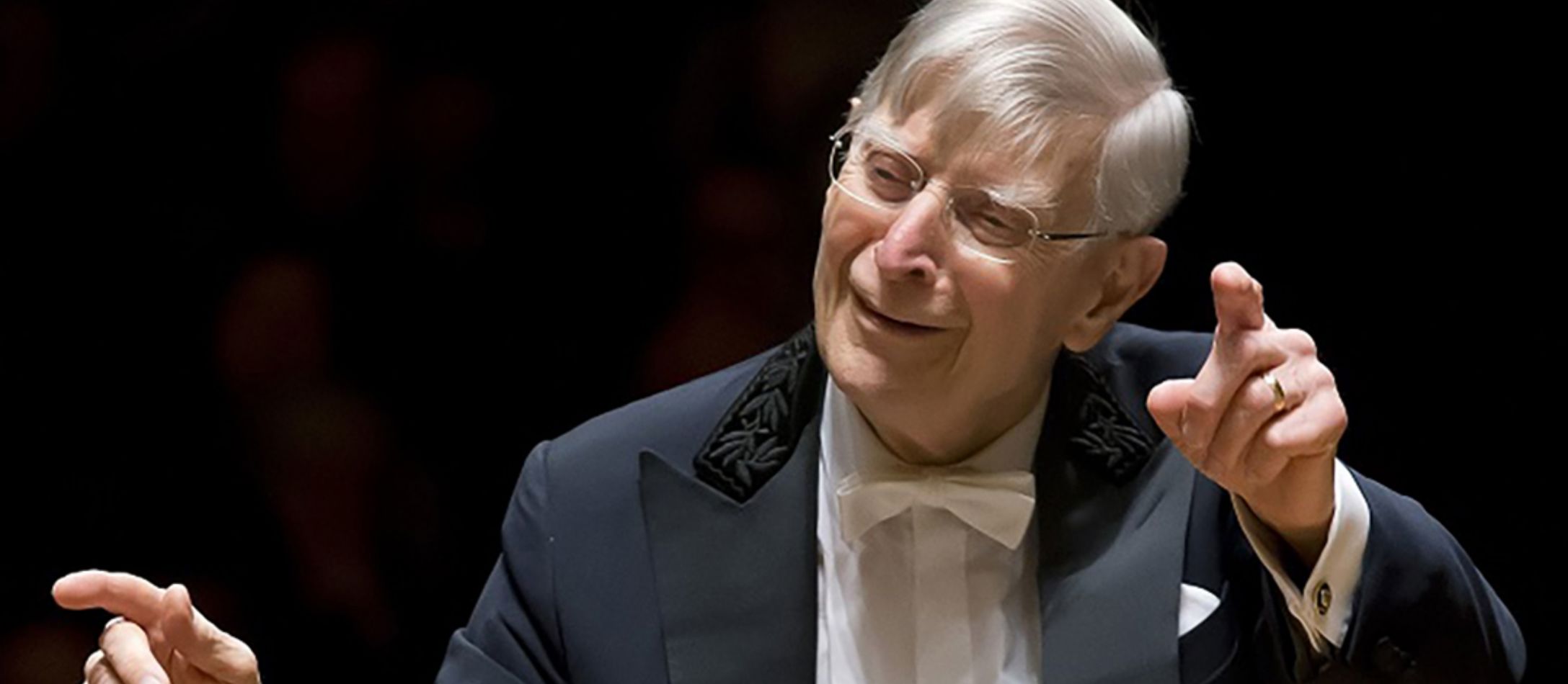 Mand i sort blazer, hvid skjorte og hvid butterfly, dirigere orkesteret.