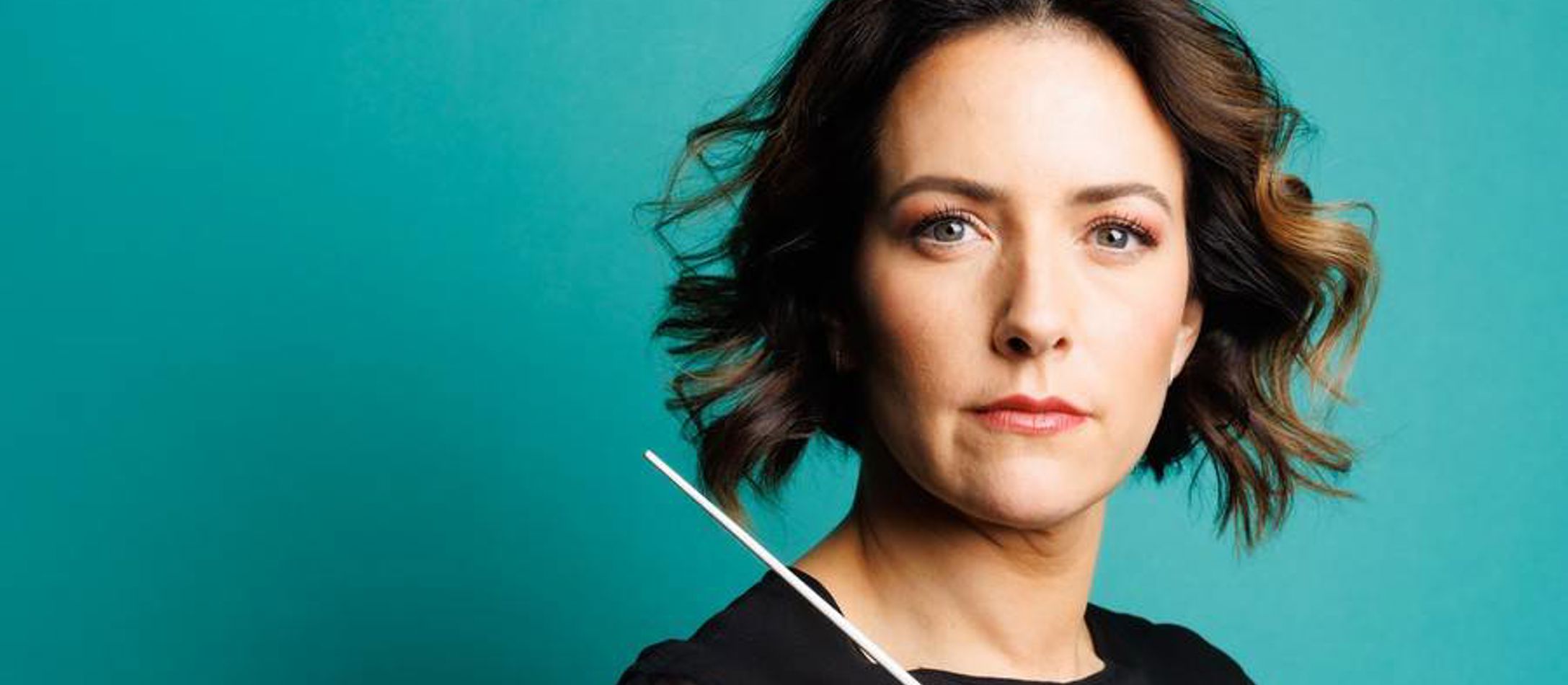 Alondra De La Parra med dirigentstav foran turkis baggrund