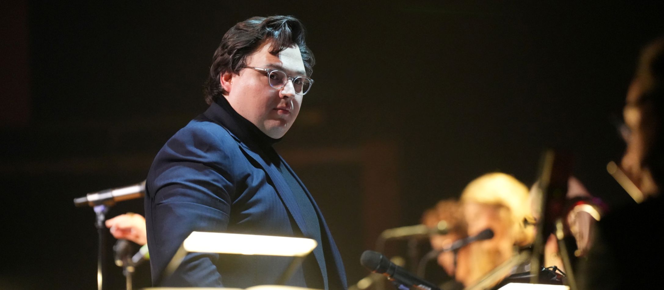 Mand står foran orkester og dirigerer.