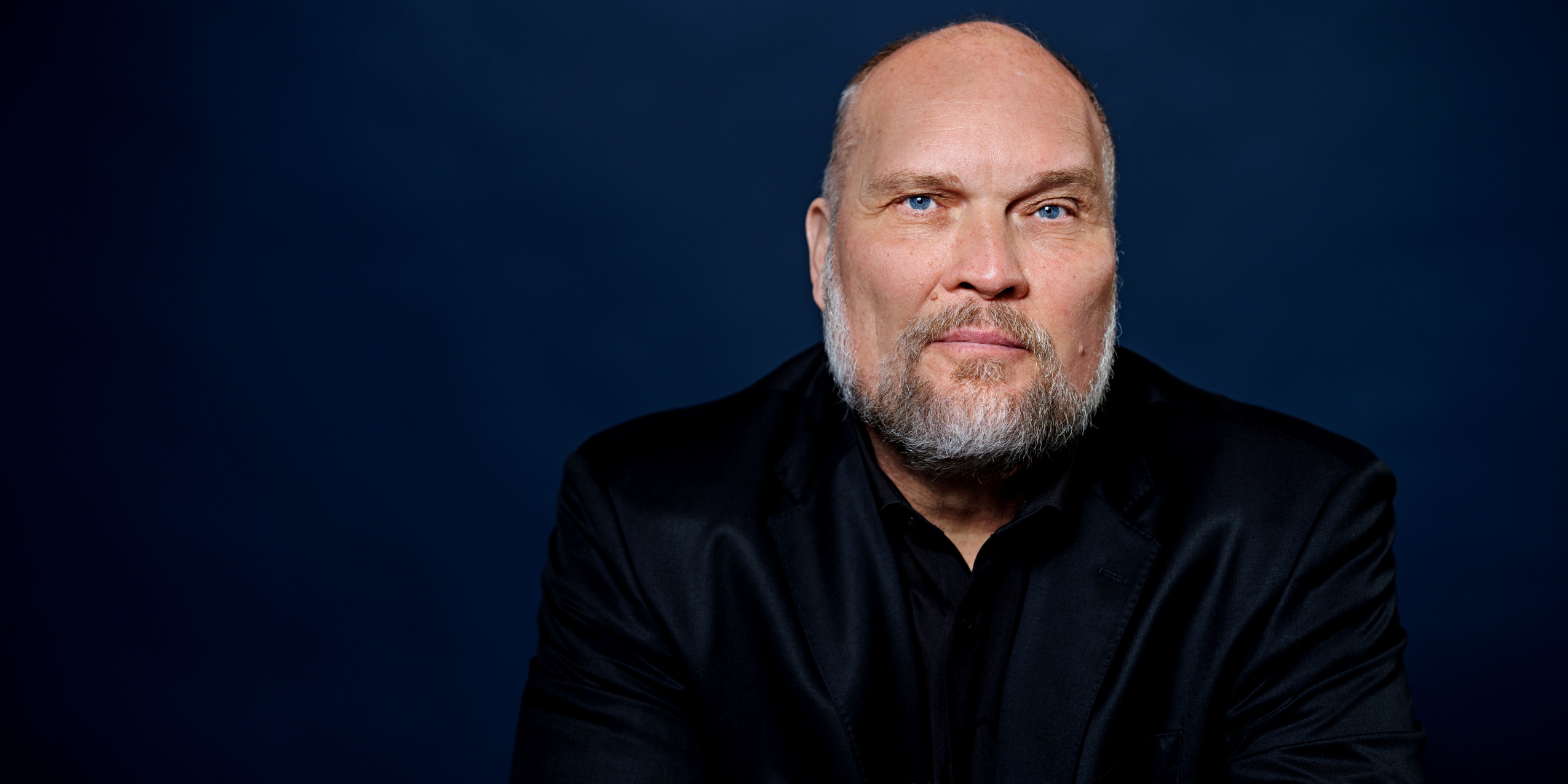 Mand i sort kigger ind i kameraet foran mørkeblå baggrund